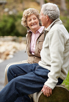 Happy mature couple sitting on log in countryside