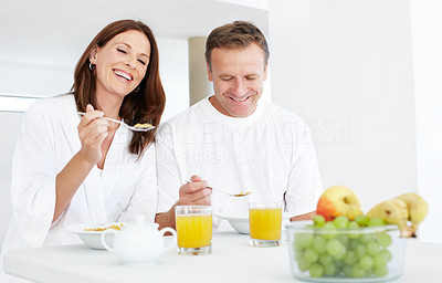 A happy couple sitting in their kitchen eating cereal for breakfast