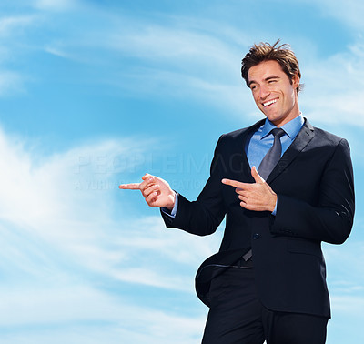 Happy business man points at something imaginary on cloudy sky