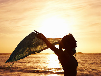 Silhouetted woman holding shawl while standing by sea at sunset