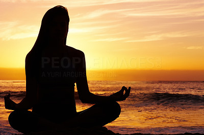 Silhouetted woman in lotus position against sea at sunset