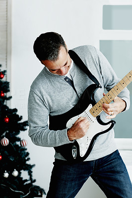 Happy mature man playing guitar with Christmas tree in background