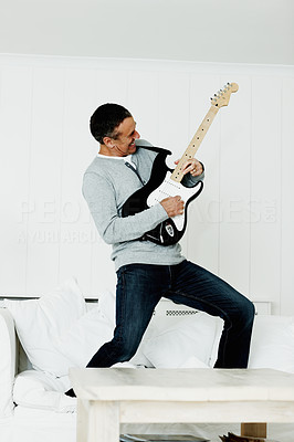Cheerful mature man standing on sofa playing an acoustic guitar