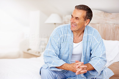 Happy mature man in bathrobe sitting on bed at home