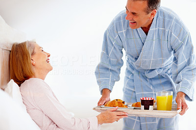 Cheerful mature woman in bed with her husband serving breakfast