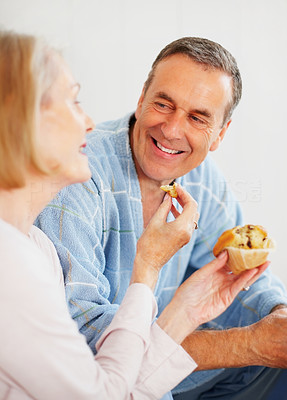 Woman feeding muffin to husband against colored background