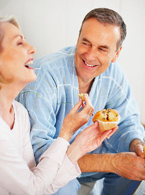 Cheerful mature woman feeding muffin to her husband