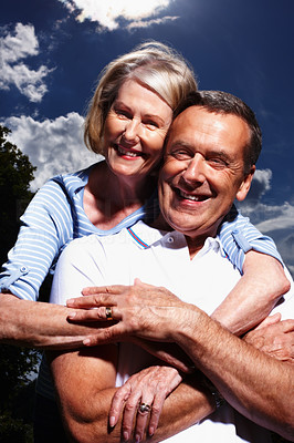 Loving mature woman hugging husband from behind against sky