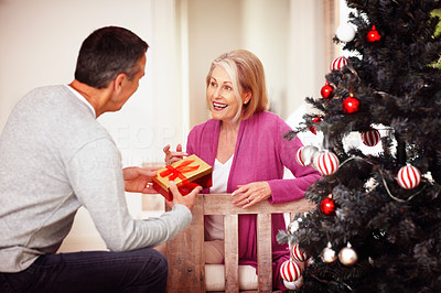 Mature man giving a Christmas present to wife at home
