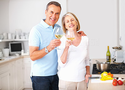 Cheerful senior couple toasting wine glasses at kitchen