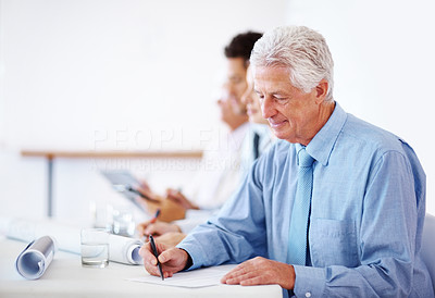 Old businessman writing notes during a meeting