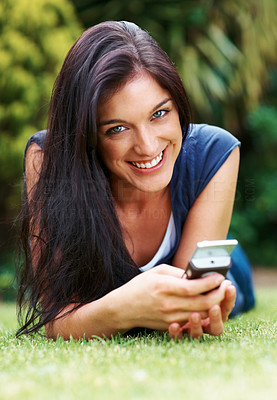 Cheerful young lady with a mobile phone lying on grass