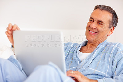 Smiling senior man with laptop on lap against white background