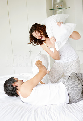 Happy mature couple fighting with pillows in bed