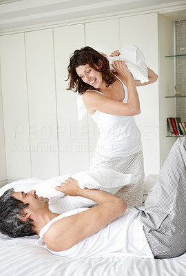 Mature man and woman fighting with pillows on bed