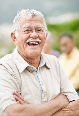 Relaxed old man laughing outdoors with people in background