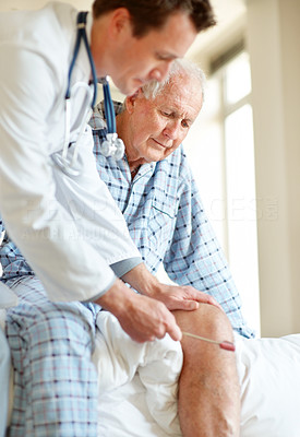 Doctor checking old man knee using a reflex hammer