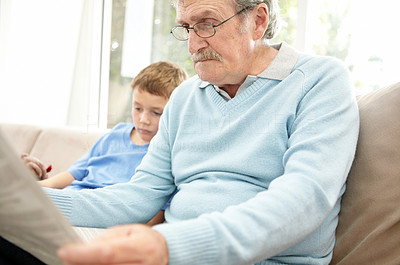 Elderly man reading newspaper with grandson in background