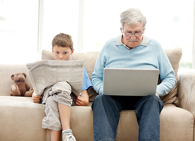 Old man using a laptop with his grand son reading a newspaper
