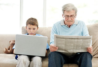 Old man reading newspaper with his grand son using laptop