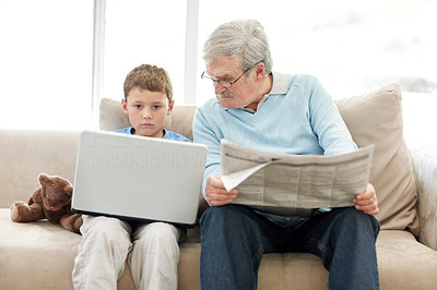 Old man sitting with a newspaper while a little boy using a laptop