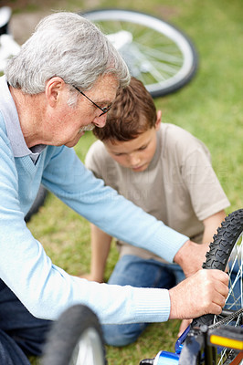 Elderly man repairing his grandson \'s cycle in a park