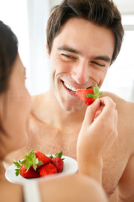 Cute young woman feeding strawberry to her husband