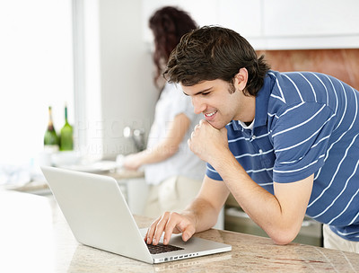 Young guy with laptop at the kitchen with female at the back