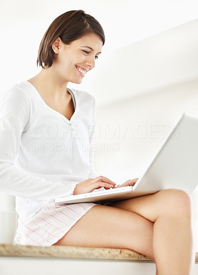 Cute female using a laptop and sitting on the kitchen counter