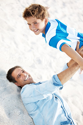 Father lying down and holding his son in air at the beach