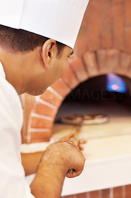 Young cook placing fresh pizza in wood fire oven