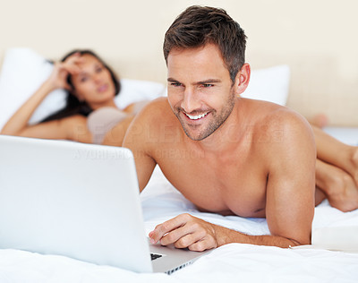 Man using laptop in bed with bored woman