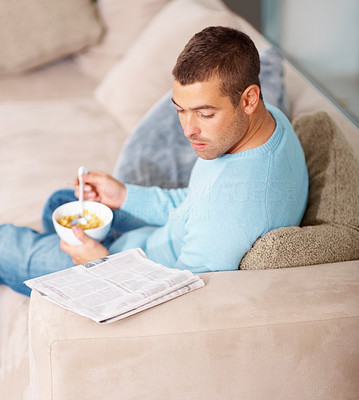 Young guy reading newspaper and eating cereal