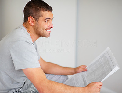 Young guy reading newspaper while looking away