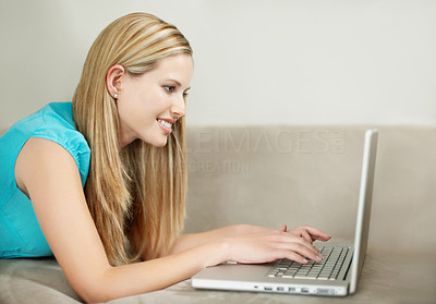 Side view of a young happy female using laptop on couch