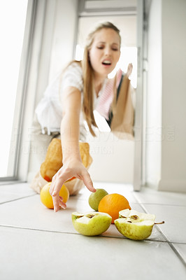 Young woman picking up fruits from floor at home