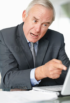 An angry mature business man pointing towards laptop