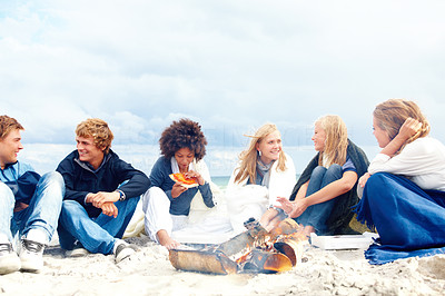 Young friends sitting at a beach and having food