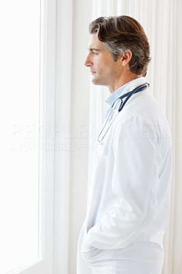 Side view of a doctor standing in thought by the window