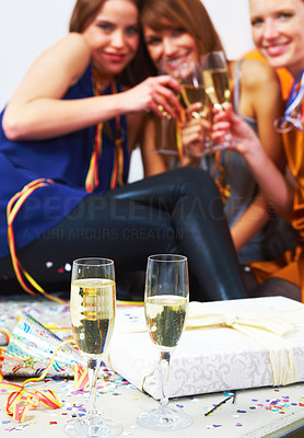 Closeup of two champagne glasses with three women in the background