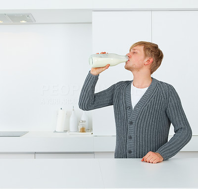 Young male drinking milk from the bottle in kitchen
