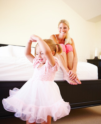 Mother sitting on bed and looking at daughter dance
