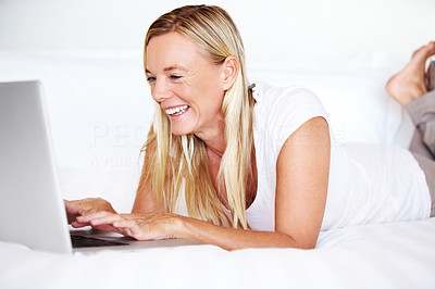 Happy mature woman lying on bed using laptop