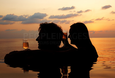 Silhouettes of a mature couple with drinks in pool