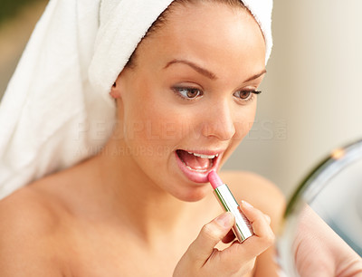 A beautiful young woman applying lipstick in the mirror