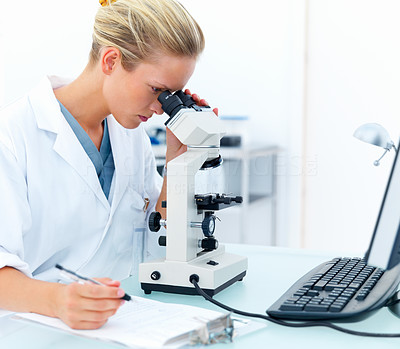 Female researcher looking into a microscope and writing notes at laboratory