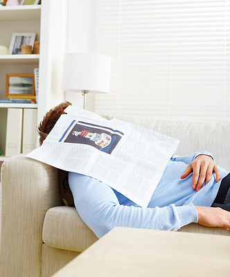 Man in house sleeping on sofa with newspaper over face