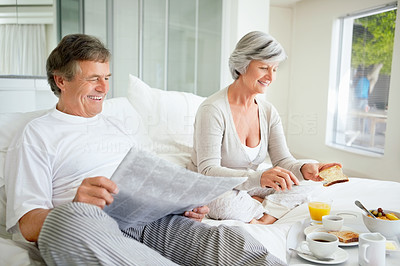 Man reading newspaper while woman preparing breakfast