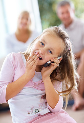 Excited young girl talking on mobile with her parents in background