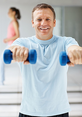 Smiling mature man using dumbbells at the gym